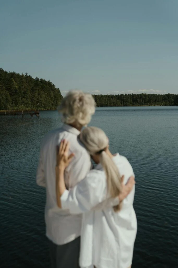 A senior man and woman holding each other while standing on a dock overlooking a lake