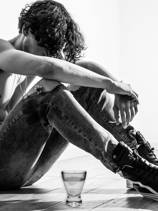 Young man sitting on the floor with head down next to a bottle and glass of alcohol, symbolizing the struggle before taking small steps to sobriety