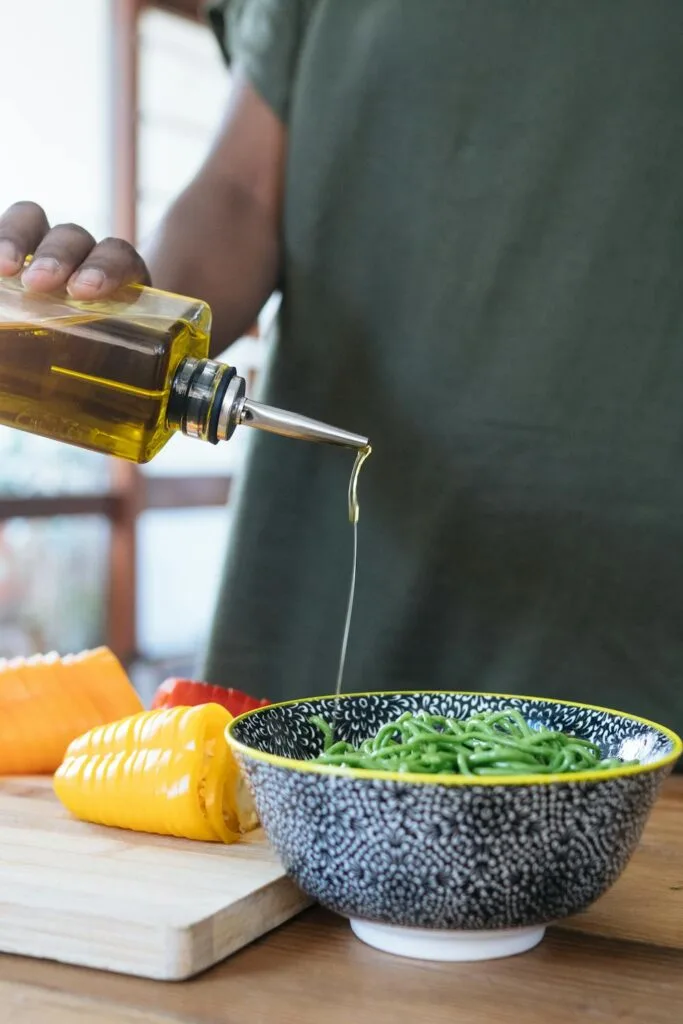 Person using olive oil for dressing on noodles