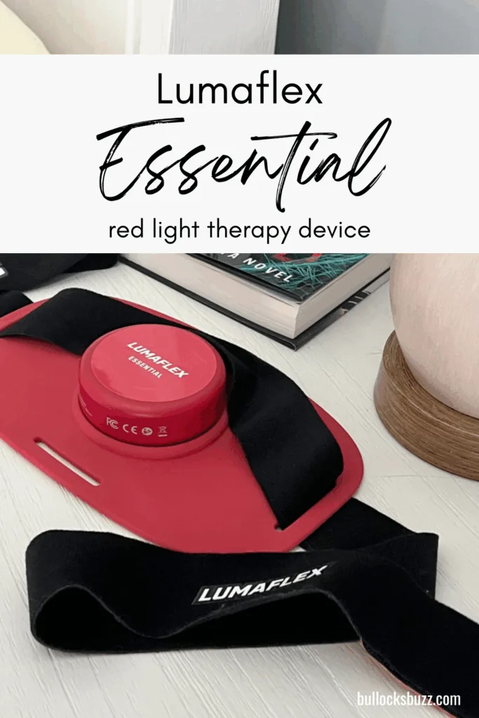 Lumaflex Essential red light therapy device with straps, shown on a desk beside a book and lamp