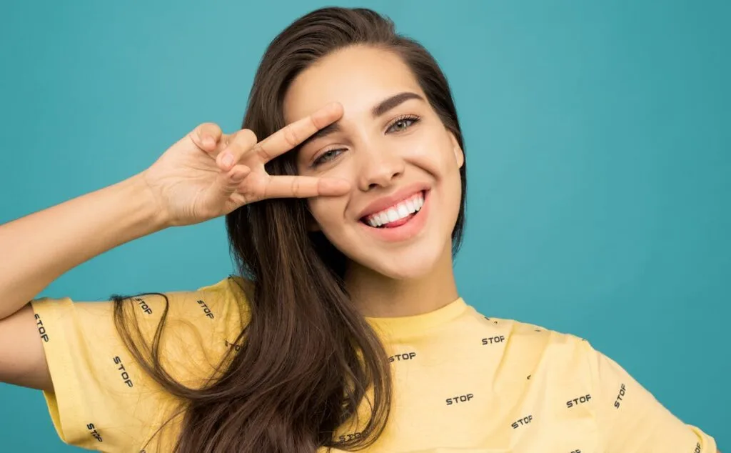 Happy young woman flashing a bright smile and making a peace sign with her fingers, showcasing her confidence and healthy teeth