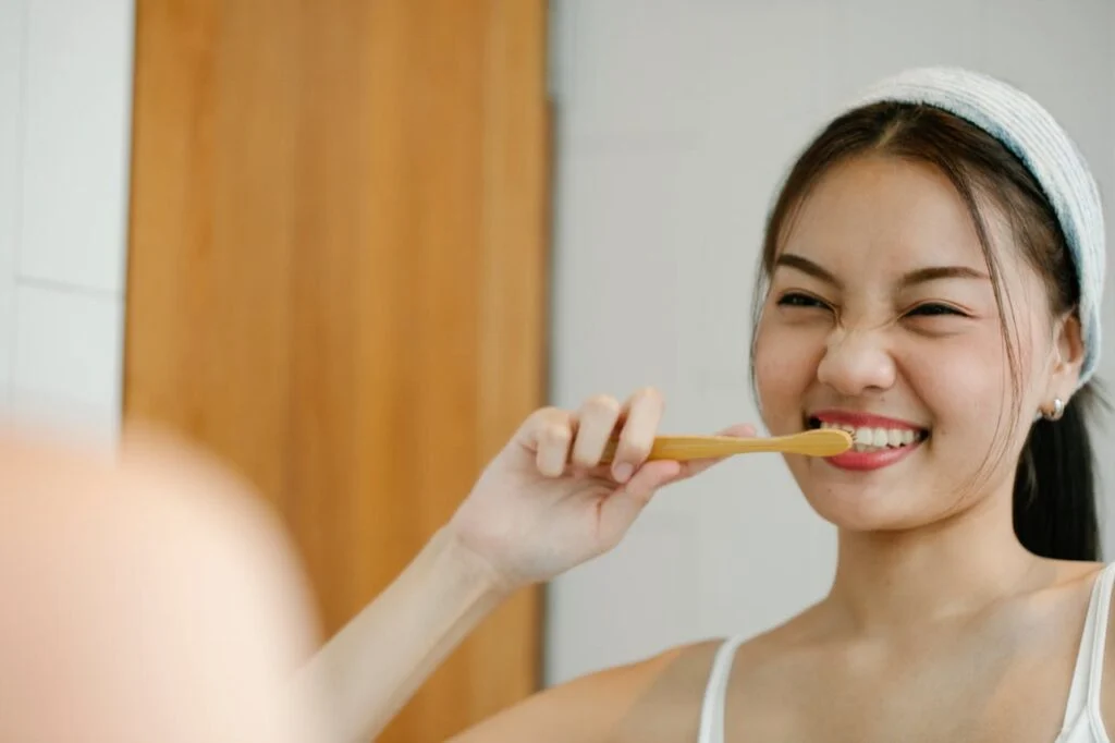 Positive woman brushing her teeth with a bamboo toothbrush, practicing oral care and bright smile tips for healthier teeth.