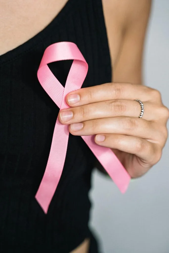 Close-up of a person holding a pink ribbon, symbolizing breast cancer awareness and support.