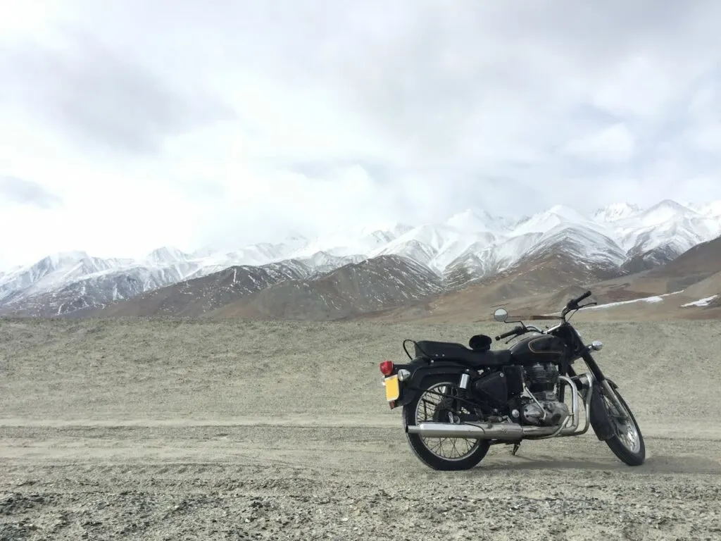 A classic black motorcycle parked on a rugged mountain road with snow-capped peaks in the background &mdash; perfect for choosing the right motorcycle for adventurous rural rides