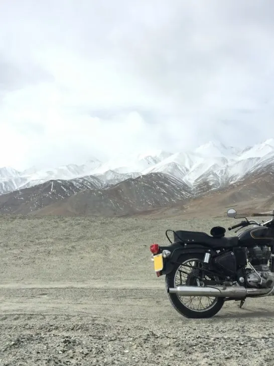 A classic black motorcycle parked on a rugged mountain road with snow-capped peaks in the background &mdash; perfect for choosing the right motorcycle for adventurous rural rides