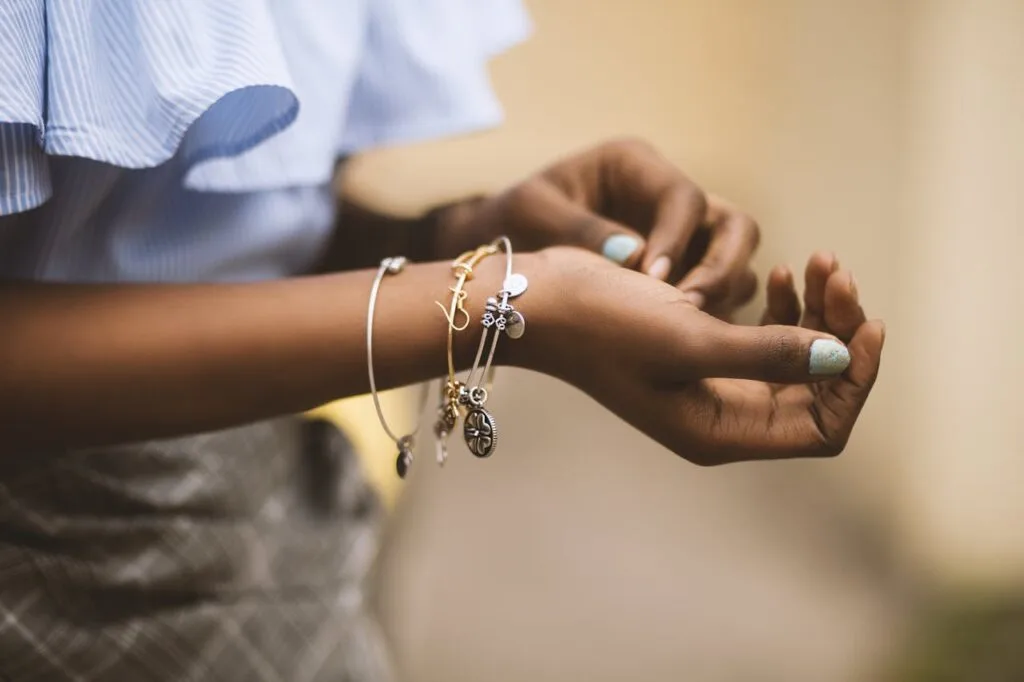 Close-up of a person&rsquo;s hands wearing layered jewelry bracelets with charms, showcasing a stylish stacked look.