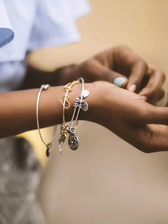 Close-up of a person&rsquo;s hands wearing layered jewelry bracelets with charms, showcasing a stylish stacked look.