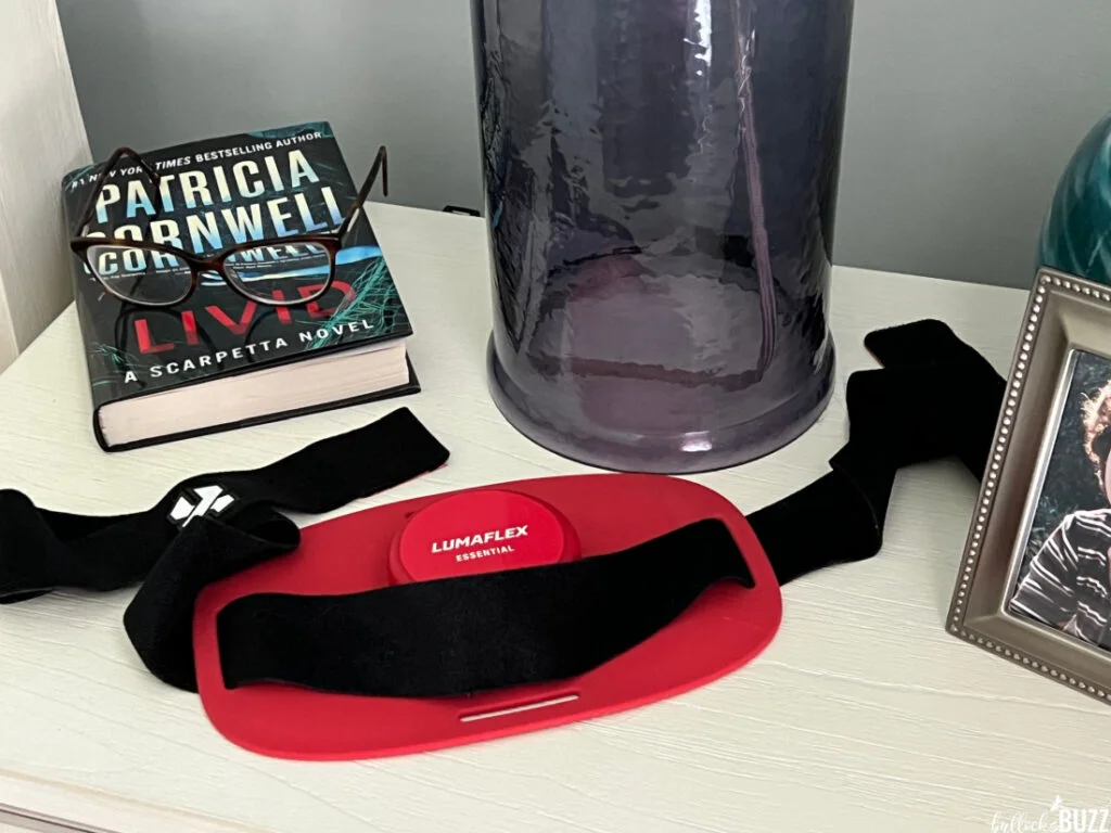 Lumaflex right light therapy device sitting next to a book and a lamp on a nightstand