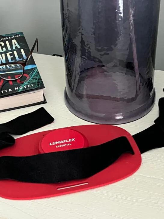 Lumaflex right light therapy device sitting next to a book and a lamp on a nightstand