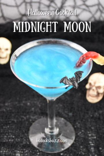 Close up picture of a sparkling blue Midnight Moon Halloween Cocktail with bat and gummy worm garnishes