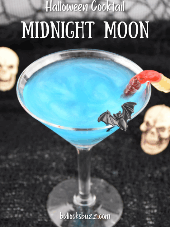 Close up picture of a sparkling blue Midnight Moon Halloween Cocktail with bat and gummy worm garnishes
