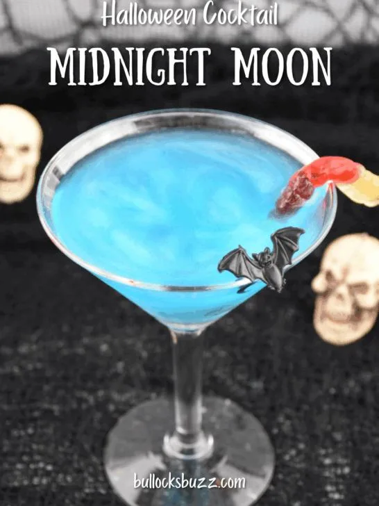 Close up picture of a sparkling blue Midnight Moon Halloween Cocktail with bat and gummy worm garnishes