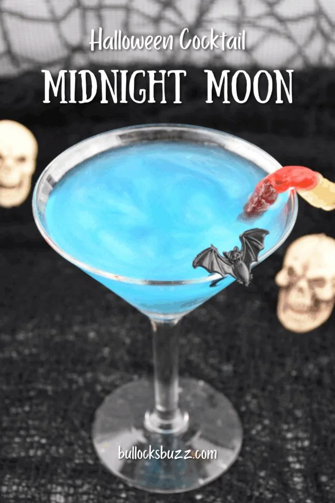 Close up picture of a sparkling blue Midnight Moon Halloween Cocktail with bat and gummy worm garnishes