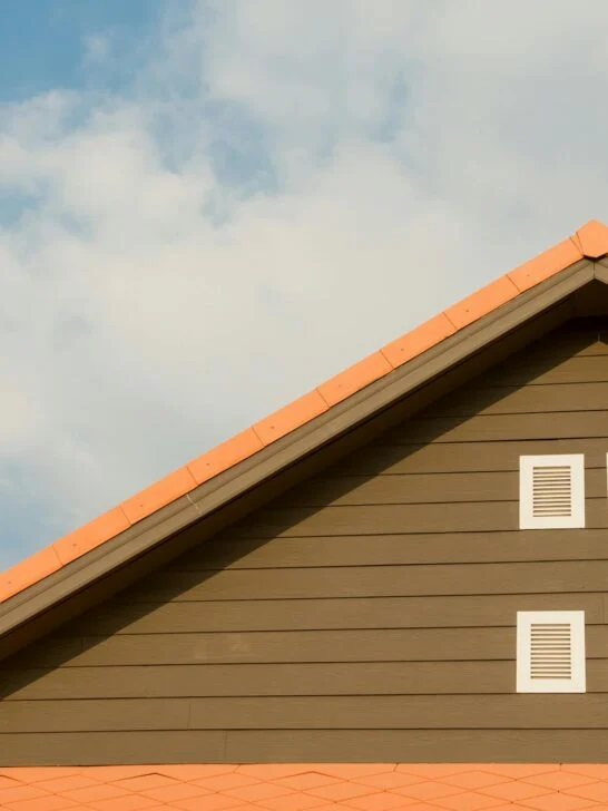 Sloped brown house roof with orange shingles and two white vents under a blue sky, illustrating roof safety tips for homeowners.