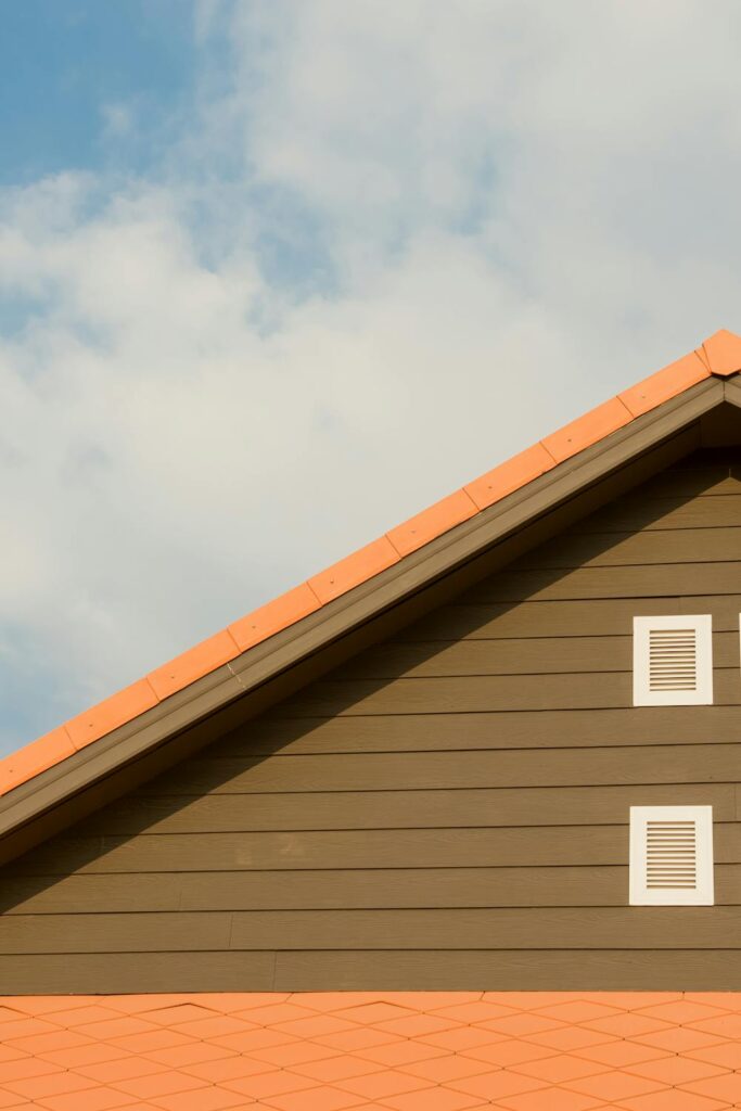 Sloped brown house roof with orange shingles and two white vents under a blue sky, illustrating roof safety tips for homeowners.