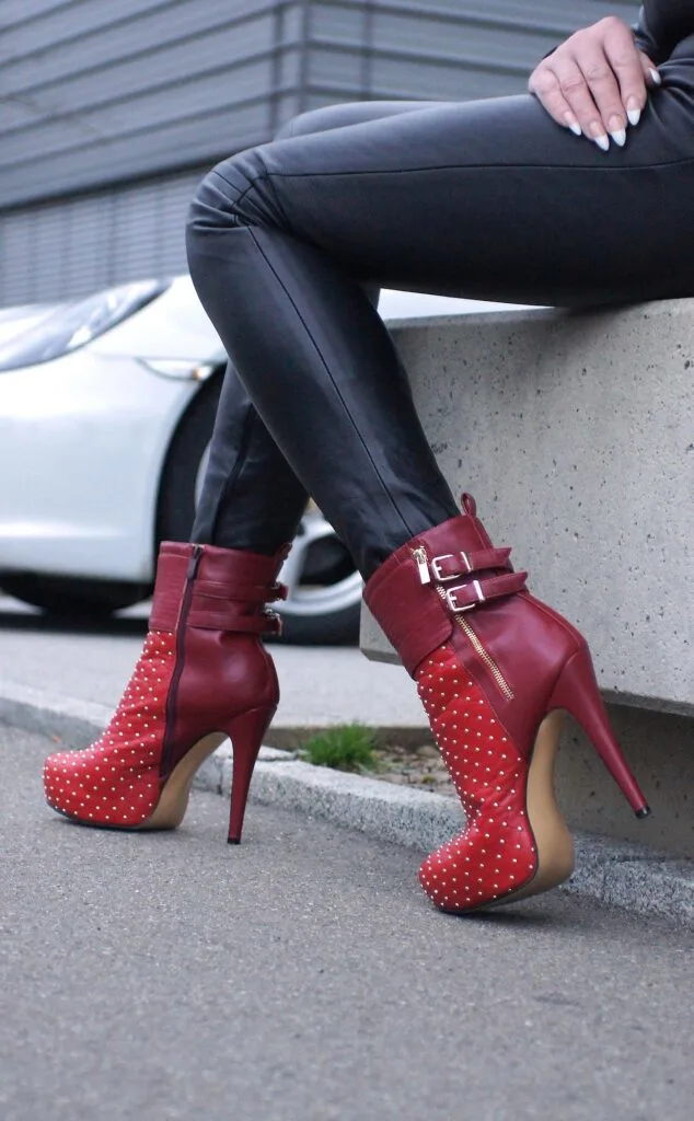 A woman wearing heeled boots in red while sitting on a concrete bench
