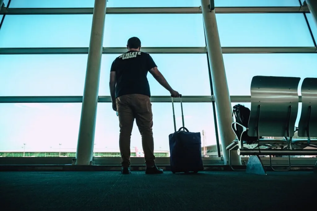 Traveler standing at airport window with luggage, waiting during a long flight delay