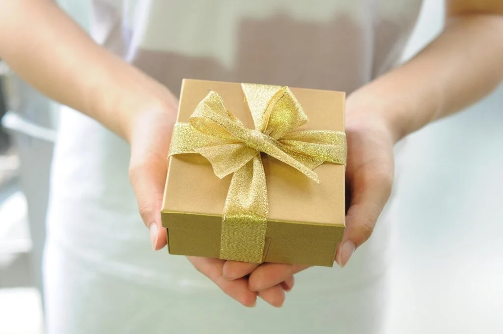 Close-up of hands holding a small gold gift box with a shimmering bow, symbolizing thoughtful, heartfelt giving.