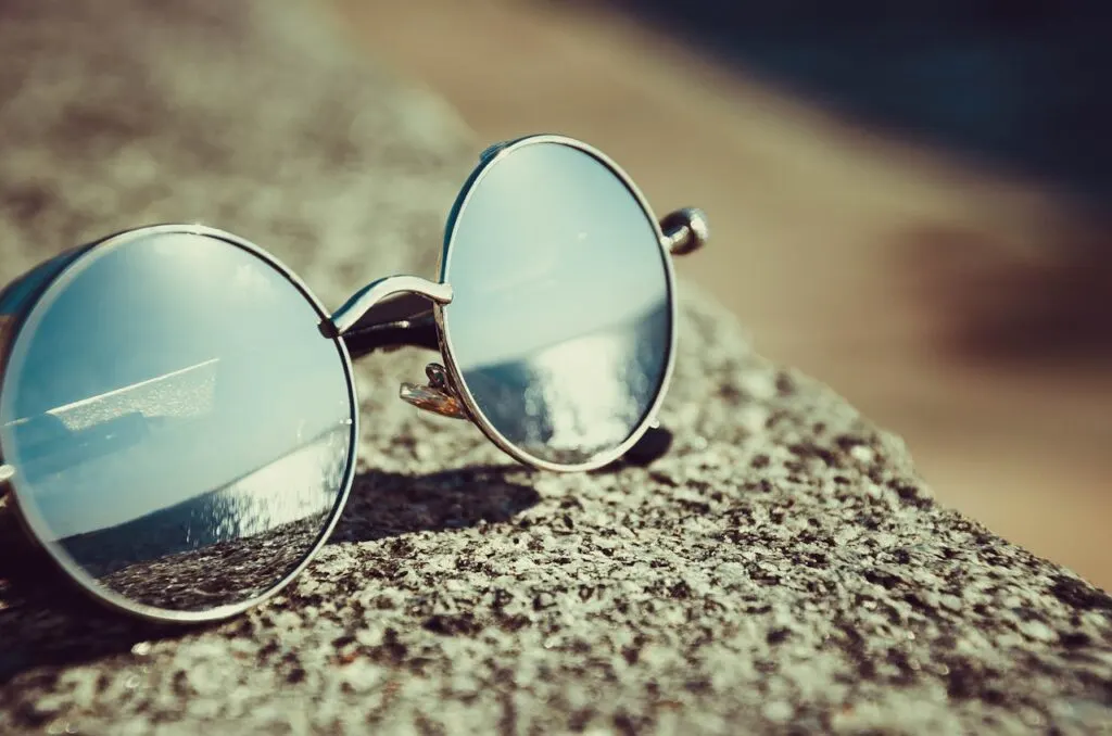 Round sunglasses resting on a stone surface, reflecting sunlight&mdash;symbolizing eye protection and sports vision training for athletes.