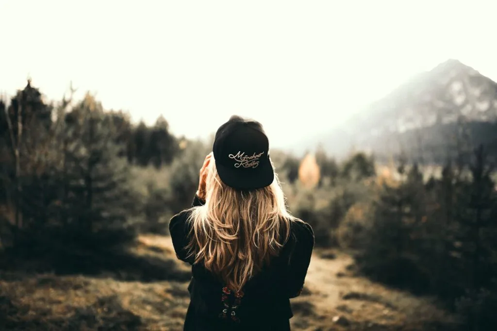 Woman standing in nature wearing a black hat, symbolizing peace, mindfulness, and reconnecting with life during recovery from a injury.