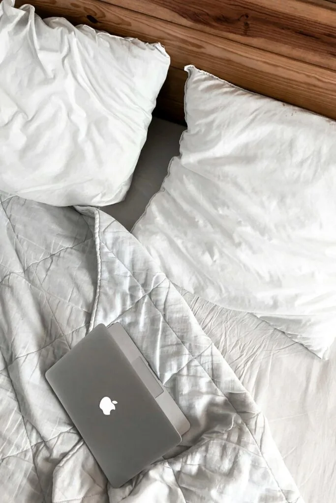 Messy bed with white bedding, laptop, and soft ergonomic pillow providing comfort for restful sleep