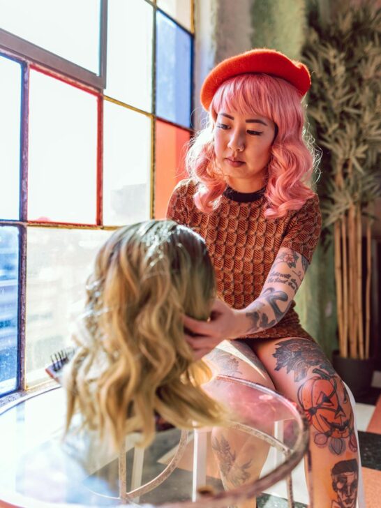 a woman with pink hair looking at a wig trying to decide how to choose the right wig for her face shape