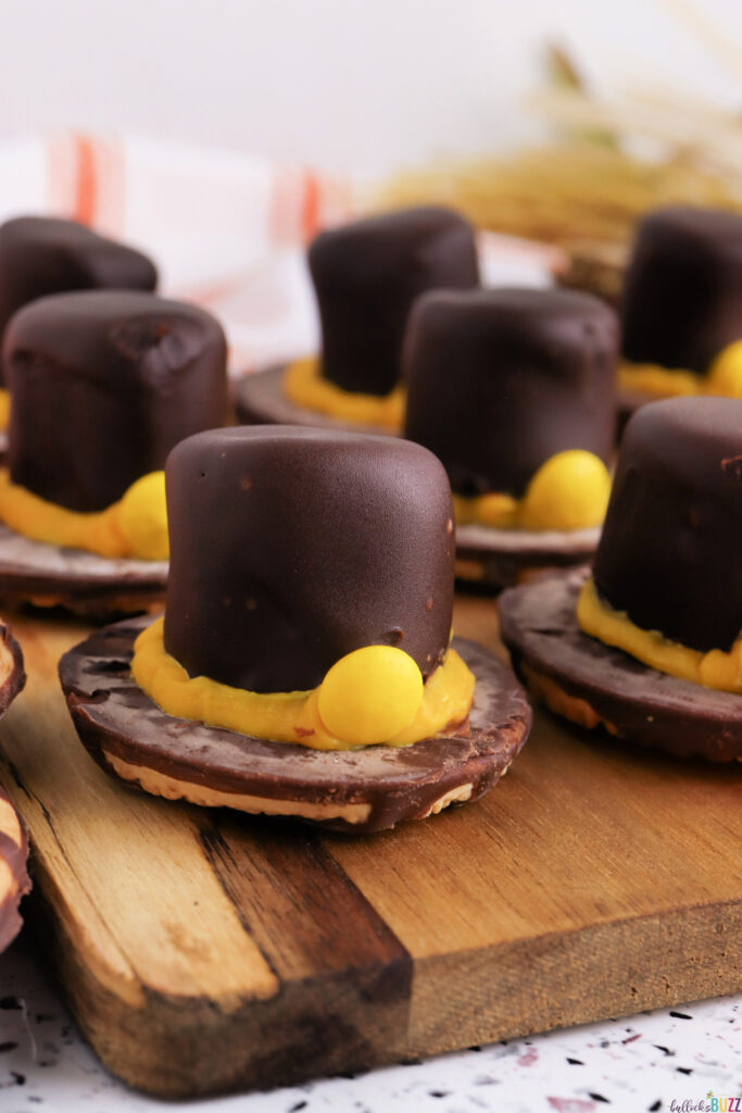 Close-up of a Fudge Stripe Pilgrim Hat Cookie topped with a chocolate-dipped marshmallow and yellow candy buckle, a fun no-bake Thanksgiving treat from Bullock’s Buzz.
