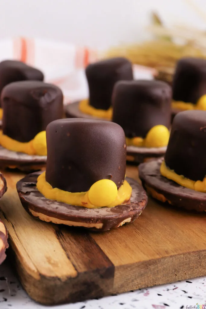 Close-up of a Fudge Stripe Pilgrim Hat Cookie topped with a chocolate-dipped marshmallow and yellow candy buckle, a fun no-bake Thanksgiving treat from Bullock’s Buzz.