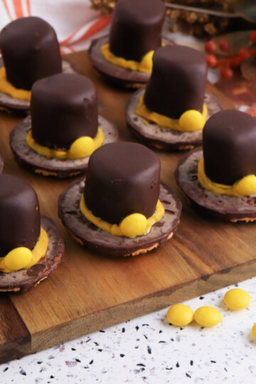 Easy no-bake Fudge Stripe Pilgrim Hat Cookies topped with chocolate-dipped marshmallows and yellow candy decorations, a festive Thanksgiving dessert idea from Bullock’s Buzz
