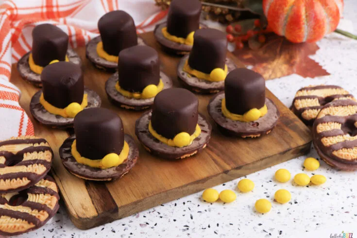 Easy no-bake Fudge Stripe Pilgrim Hat Cookies topped with chocolate-dipped marshmallows and yellow candy decorations, a festive Thanksgiving dessert idea from Bullock’s Buzz