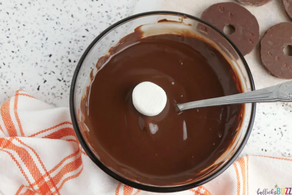 Marshmallow being dipped into melted chocolate for Pilgrim hat cookies