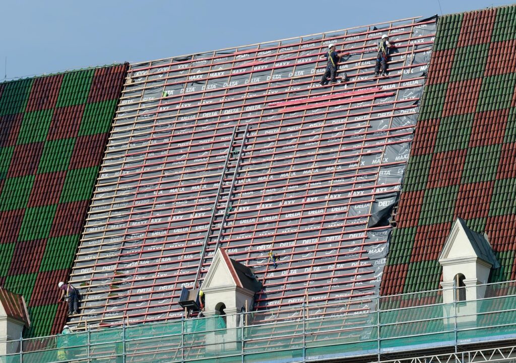 Construction workers performing roof maintenance on a large tiled roof, reinforcing beams and preparing for new shingles.