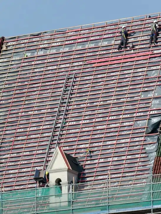 Construction workers performing roof maintenance on a large tiled roof, reinforcing beams and preparing for new shingles.