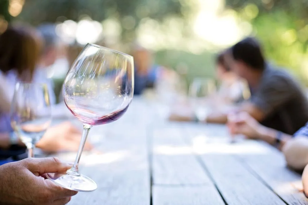 A guest holding a glass of red wine at an outdoor table during a relaxed Gatlinburg wine tasting experience, surrounded by people enjoying conversation in the Tennessee sunshine.