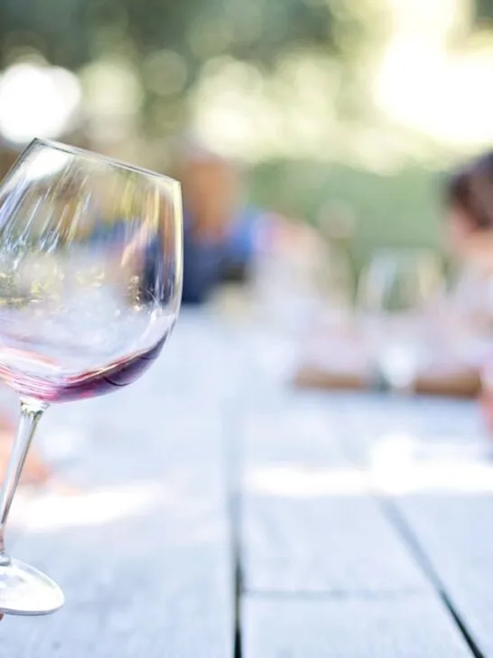A guest holding a glass of red wine at an outdoor table during a relaxed Gatlinburg wine tasting experience, surrounded by people enjoying conversation in the Tennessee sunshine.