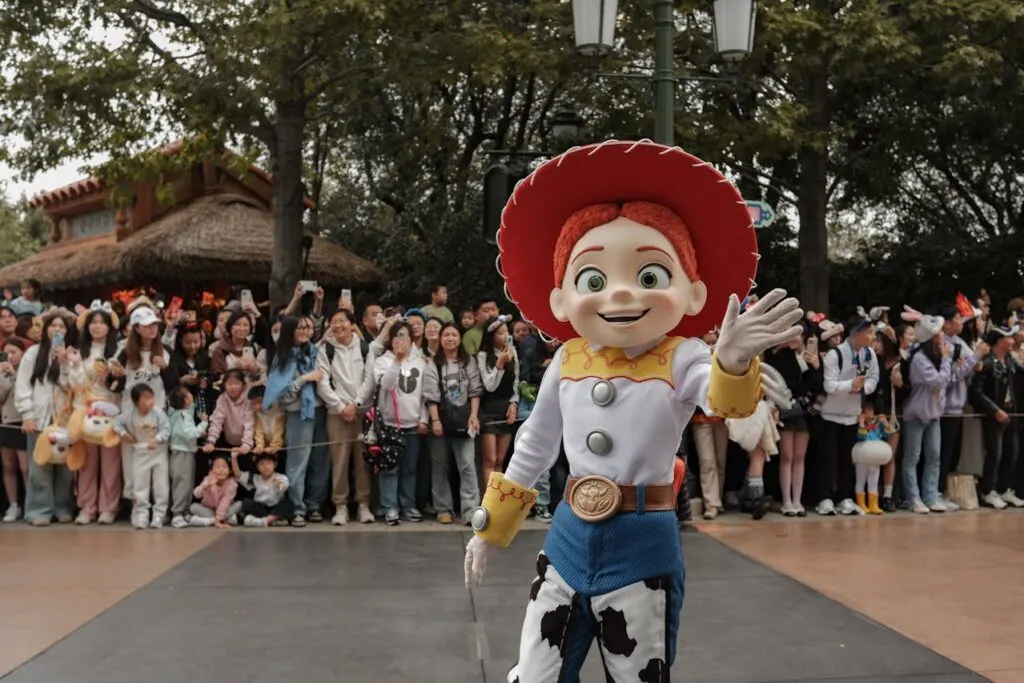 Theme park performer dressed as Jessie from Toy Story waving to a crowd of visitors during a parade.