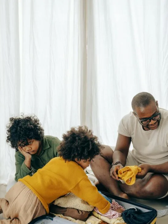 Family packing clothes for a trip, choosing coordinated pieces for family outfits for theme park vacations while sitting around an open suitcase.