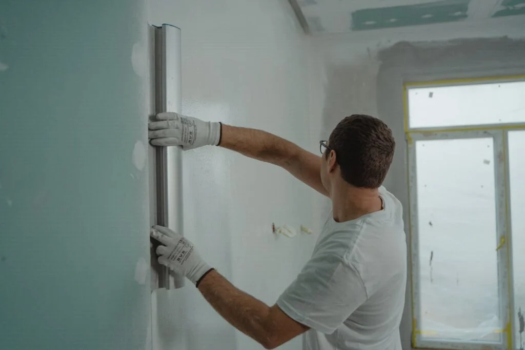 Worker smoothing a newly painted or repaired wall with a leveling tool, showing careful attention to detail during home renovations.