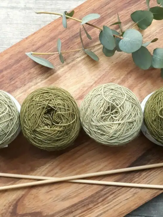 Three green yarn balls and wooden knitting needles arranged on a board, showcasing materials often included in knitting starter kits.