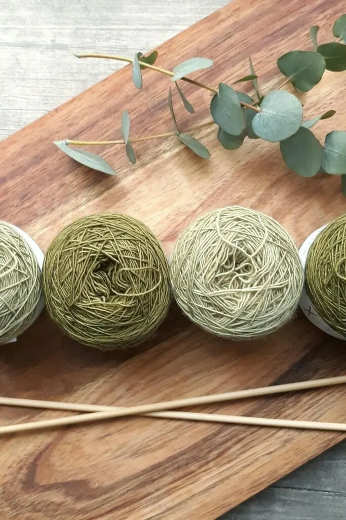 Three green yarn balls and wooden knitting needles arranged on a board, showcasing materials often included in knitting starter kits.