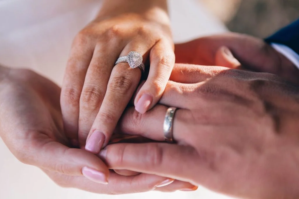Close-up of a couple&rsquo;s hands showing a diamond engagement ring and a man wearing a platinum wedding band, symbolizing timeless commitment. (Includes keyword: platinum wedding rings for men)