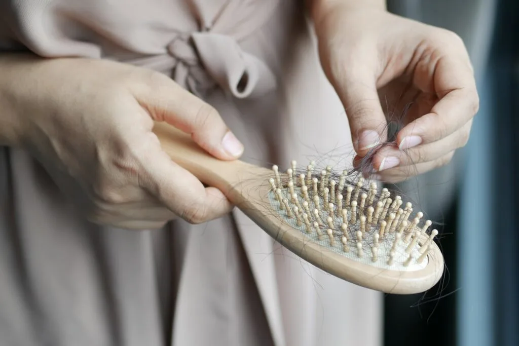 Close-up of a woman&rsquo;s hands holding a hairbrush filled with dark strands, showing signs of postpartum hair loss.