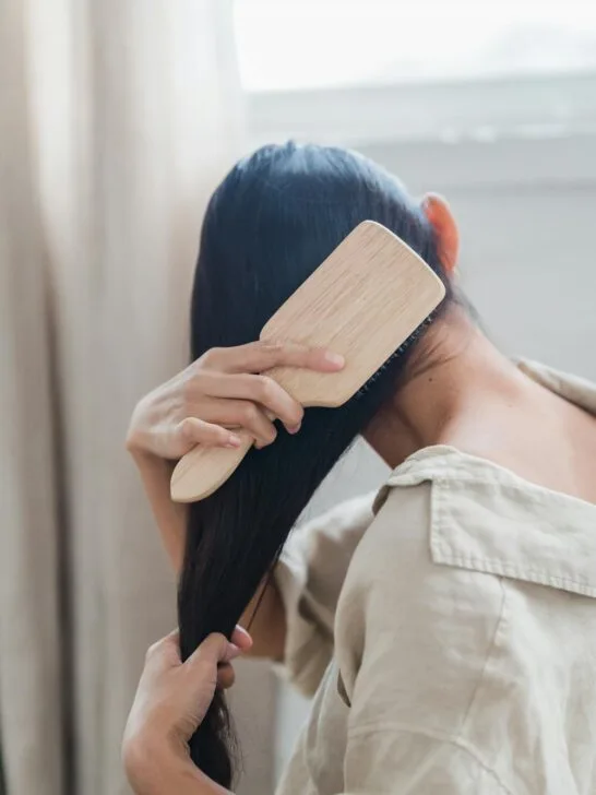 New mom brushing her hair at home while managing postpartum hair loss and embracing self-care after childbirth.