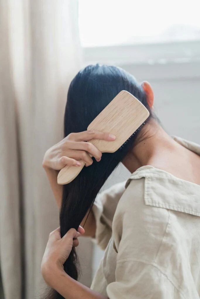 New mom brushing her hair at home while managing postpartum hair loss and embracing self-care after childbirth.