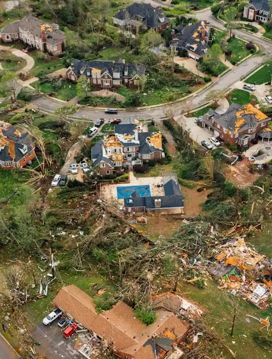 Aerial view of widespread storm damage across a residential neighborhood, showing destroyed roofs and fallen trees after rebuilding after a natural disaster begins.
