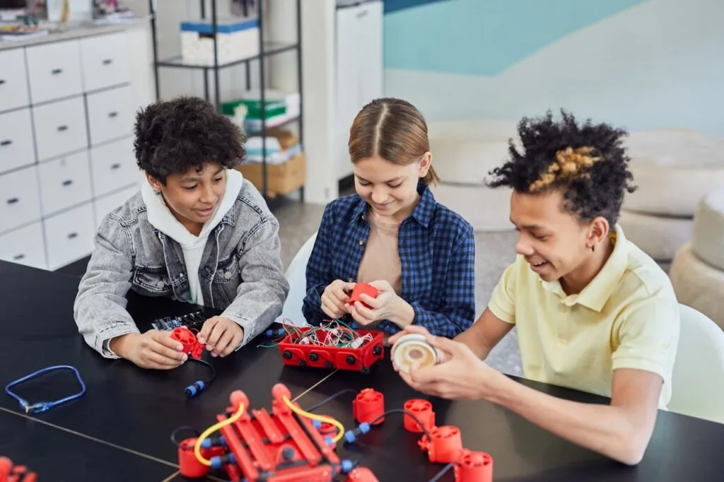 Two children focused on a paper-cutting craft activity.
Colorful shapes and scissors are spread across the table.
Each child concentrates on cutting out their own paper design.