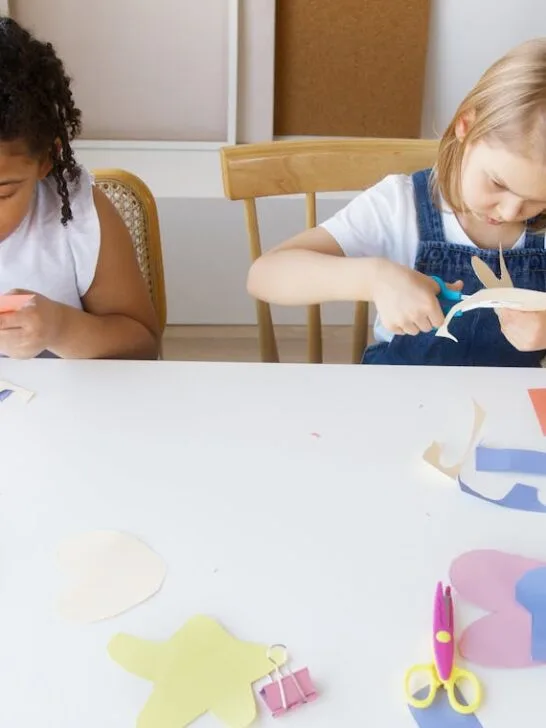 Kids working together on a robotics project at a table. They’re assembling red parts and wires while smiling and chatting. This image reflects the skills needed to work with children in STEM-based activities.