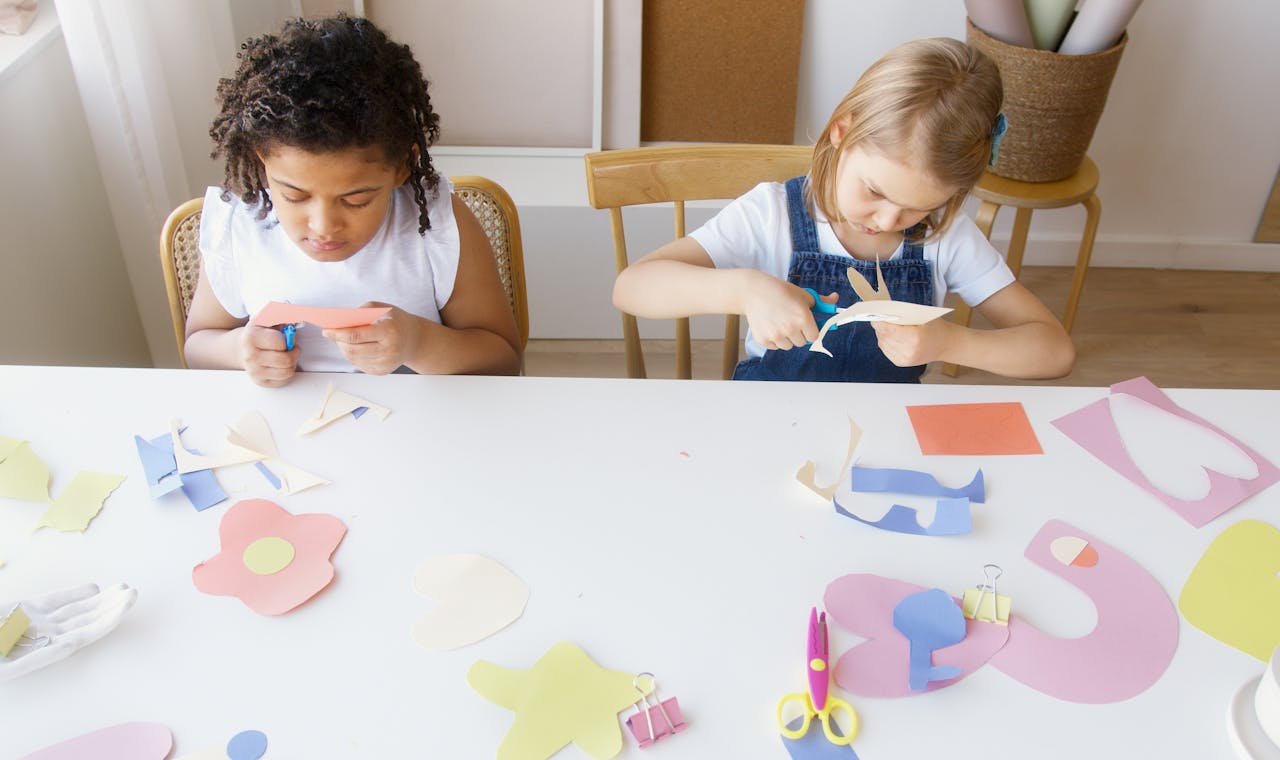 Kids working together on a robotics project at a table. They’re assembling red parts and wires while smiling and chatting. This image reflects the skills needed to work with children in STEM-based activities.