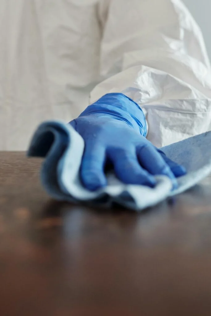 A close-up of a cleaner wearing blue gloves wiping a wooden surface, illustrating southern move out cleaning tips for tackling grime in humid climates.