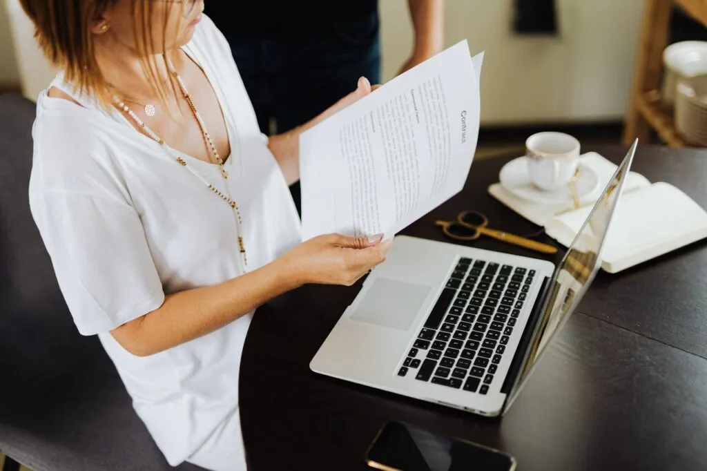 Professional reviewing documents beside a laptop at a desk, showing modern work habits and everyday business communication in action.
